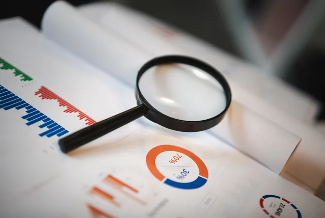 An image showcasing a magnifying glass placed on financial graphs and charts depicting statistical data. How do you work out technical SEO return on investment?